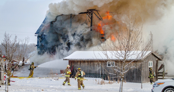 Firefighters battle a large winter barn fire using hoses.