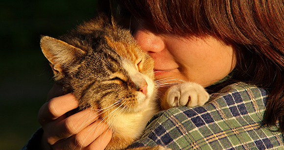A young woman wearing a plaid shirt holds a cat close to her shoulder.