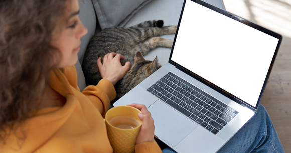 A teenager looks at her laptop while petting a cat.