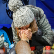 A woman crouches down while kissing her small tan dog on the head.