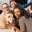 Four smiling teenagers gather around a Golden Retriever. 