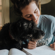 woman cuddling with dog while writing a paper