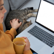 A teenager looks at her laptop while petting a cat.